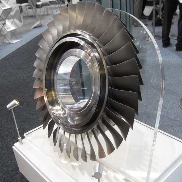 An aerospace blisk (bladed disk) component for a gas turbine engine on display at an exhibition.